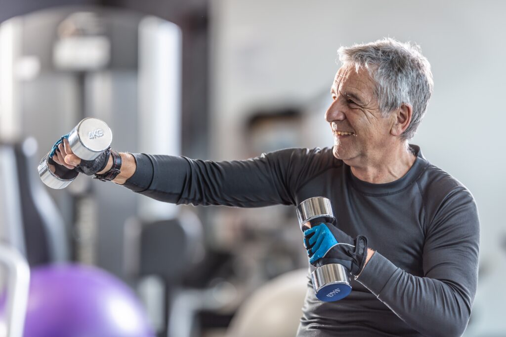 Older,Man,Working,Out,With,Dumbbells,Inside,The,Gym,,Smiling.